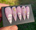 Pink stiletto press-on nails with white cloud, gold moon, and star designs
