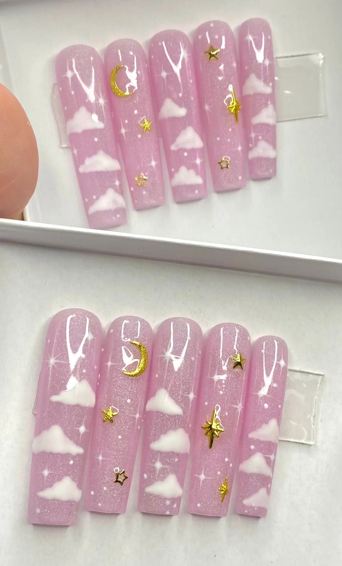 Pink press-on nails with white clouds, gold moon and stars, and glitter celestial design