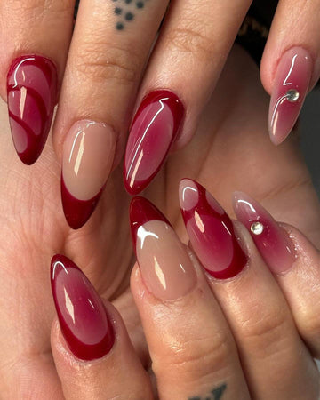Almond-shaped red and nude press-on nails with glossy finish and accent gems