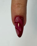 Almond-shaped press-on nail with glossy red and burgundy summer swirl design