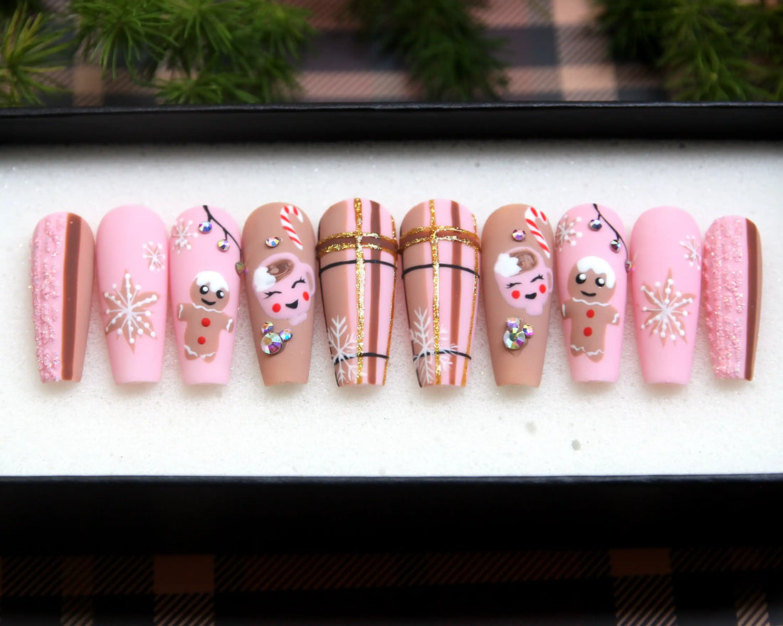 Pink Christmas press-on nails with snowflakes, gingerbread, candy cane, and crystal accents.
