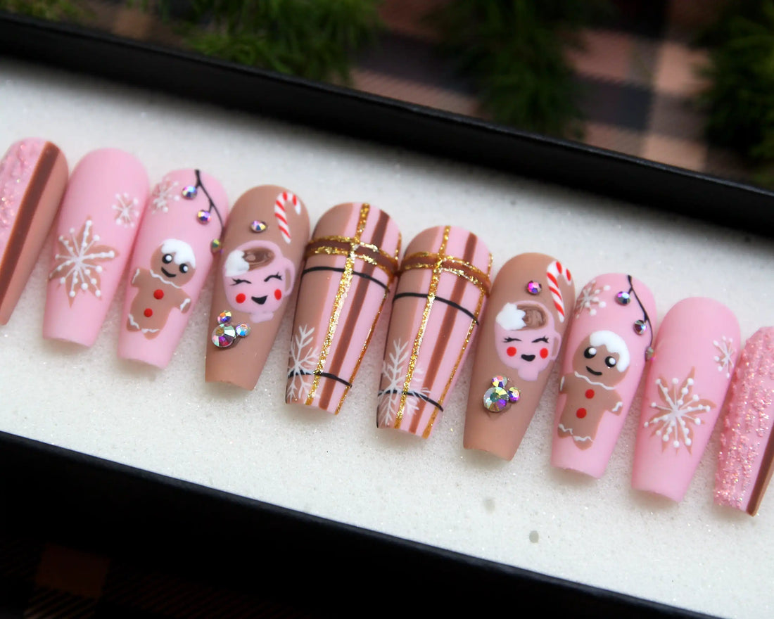 Pink Christmas press-on nails with snowflakes, gingerbread, candy cane, and crystal accents.