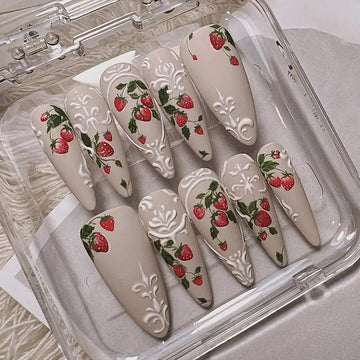 Handmade press-on nails with matte nude base, strawberry and white embossed floral designs in a case.
