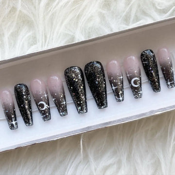 Handmade press-on nails with black ombre, glitter, moon and star designs in a box