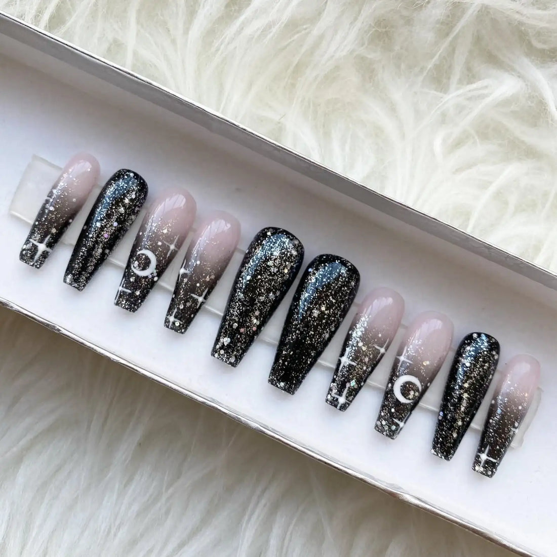 Handmade press-on nails with black ombre, glitter, moon and star designs in a box