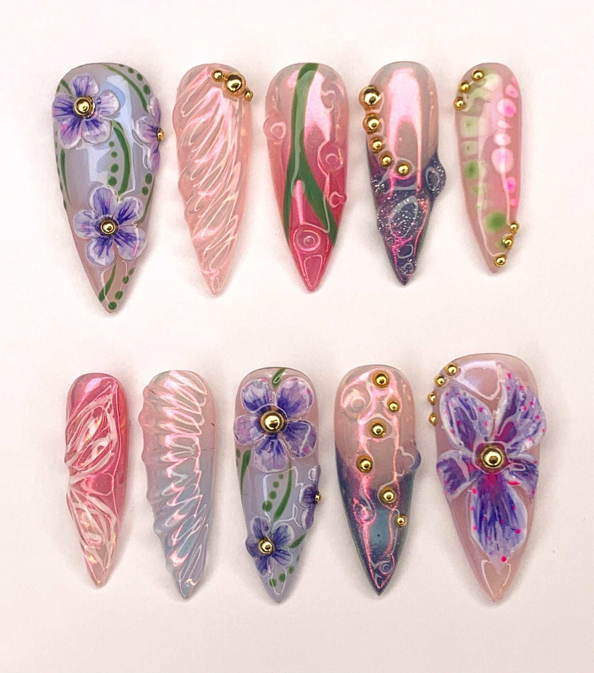 Handmade press-on nails with floral designs, gold accents, and pastel colors on display