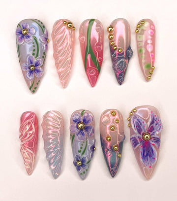 Handmade press-on nails with floral designs, gold accents, and pastel colors on display