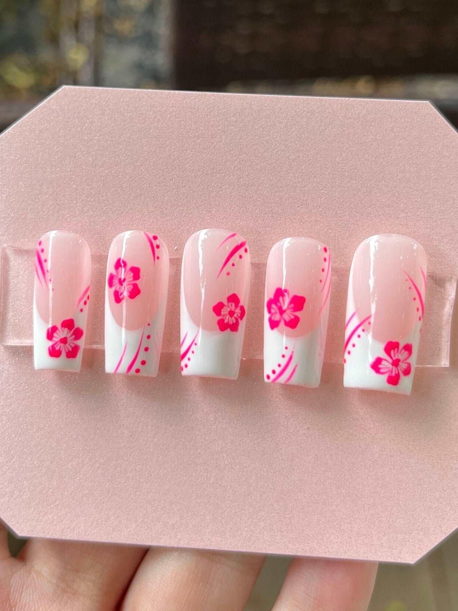 Pink and white press-on nails with floral and swirl designs, displayed on a card