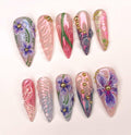 Handmade reusable press-on nails with purple floral designs, gold accents, and pink swirls