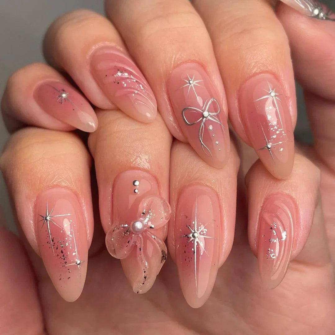 Pink almond-shaped press-on nails with silver star, bow, glitter, and 3D flower accents.
