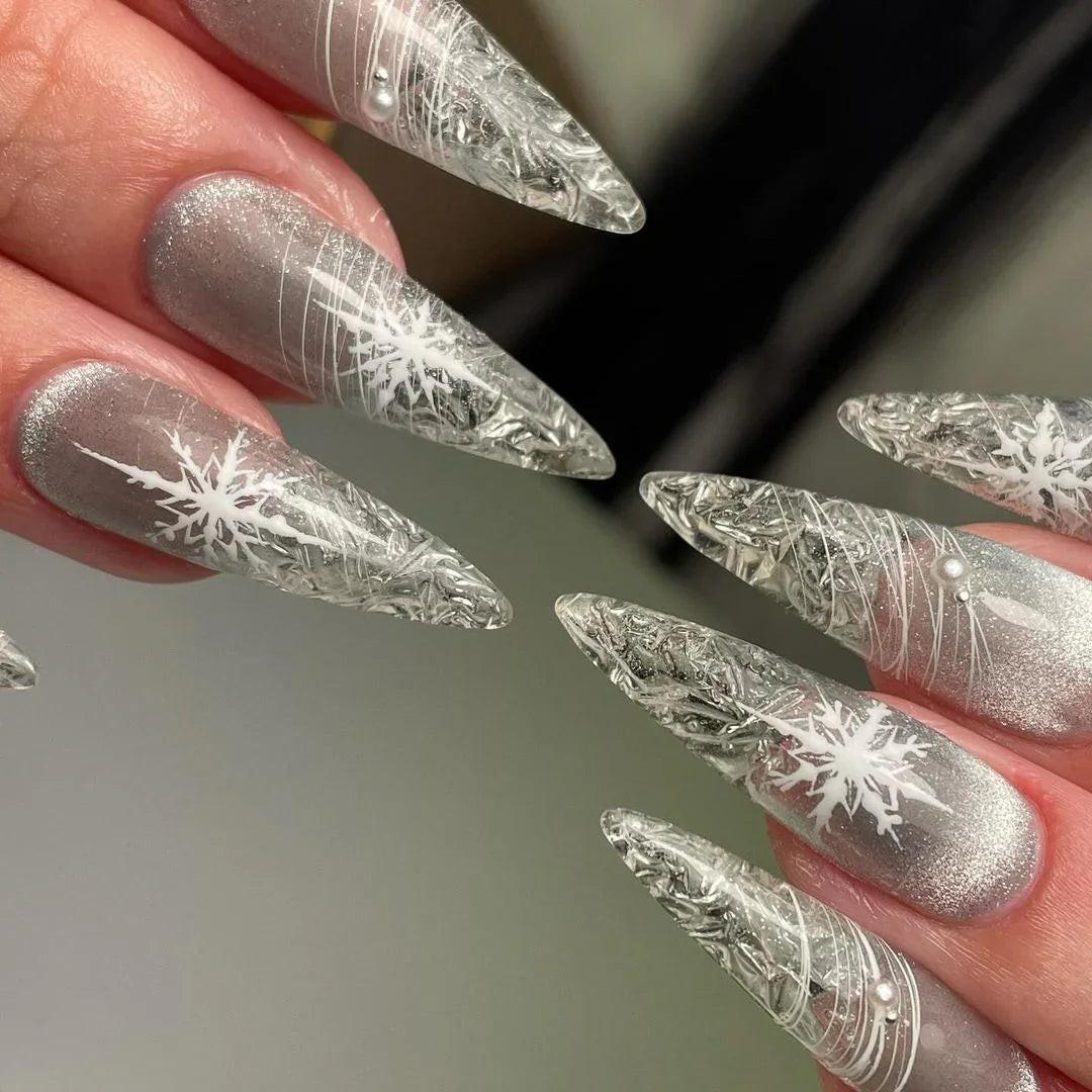 Long stiletto press-on nails with silver glitter and white snowflake nail art design