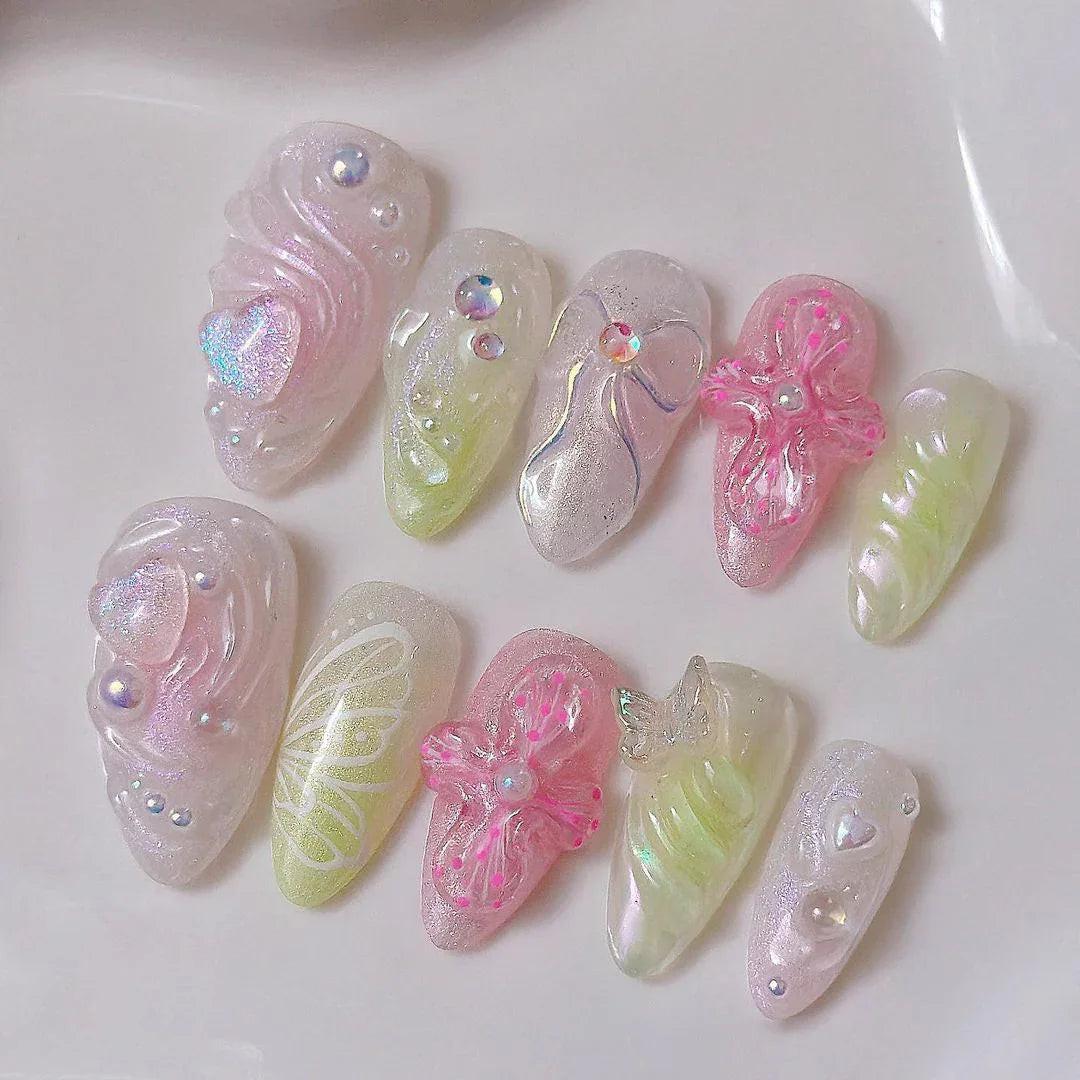 Handmade iridescent press-on nails with 3D floral, butterfly, and pearl designs on white surface