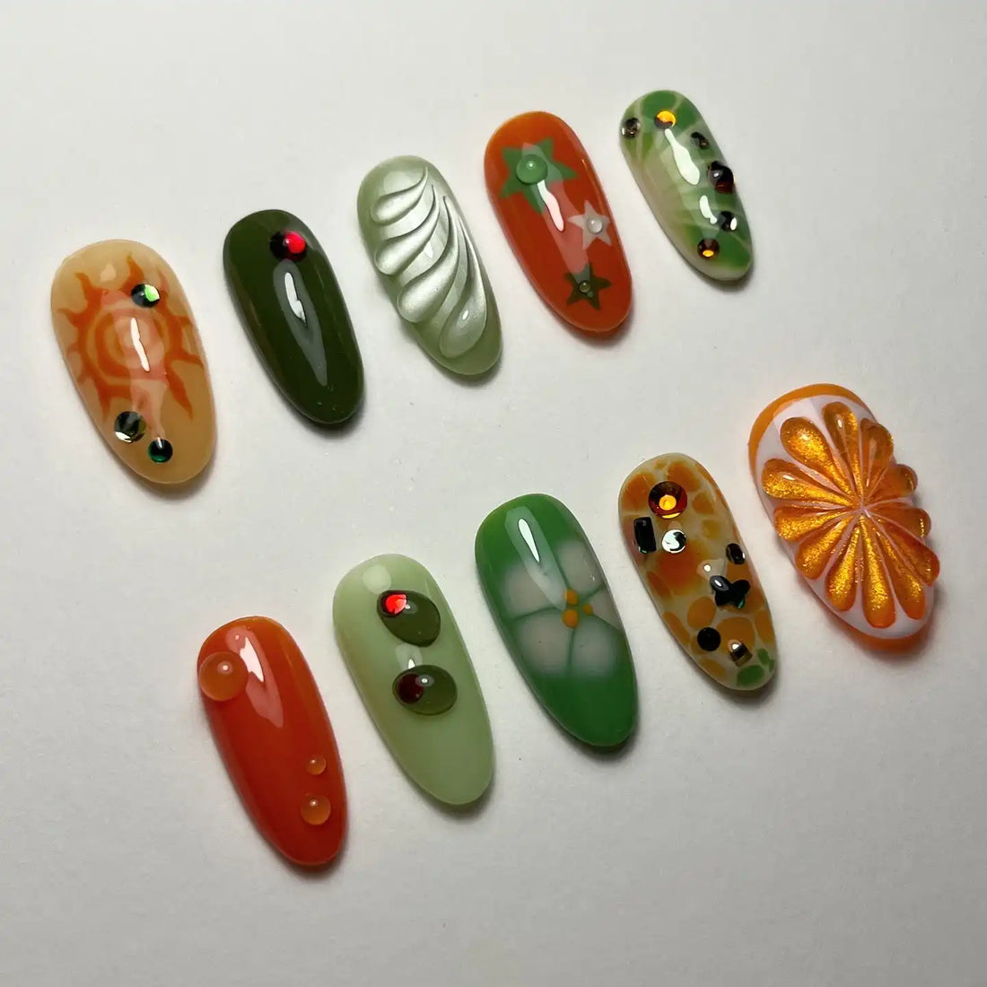 Handmade press-on nails with green and orange designs, rhinestones, and floral patterns