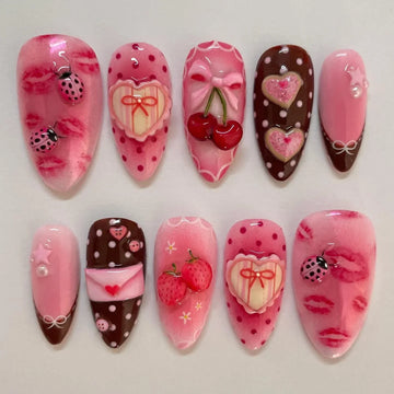 Handmade press-on nails with pink, red, and brown designs featuring ladybugs, strawberries, hearts, cherries, bows, polka dots, and lips.